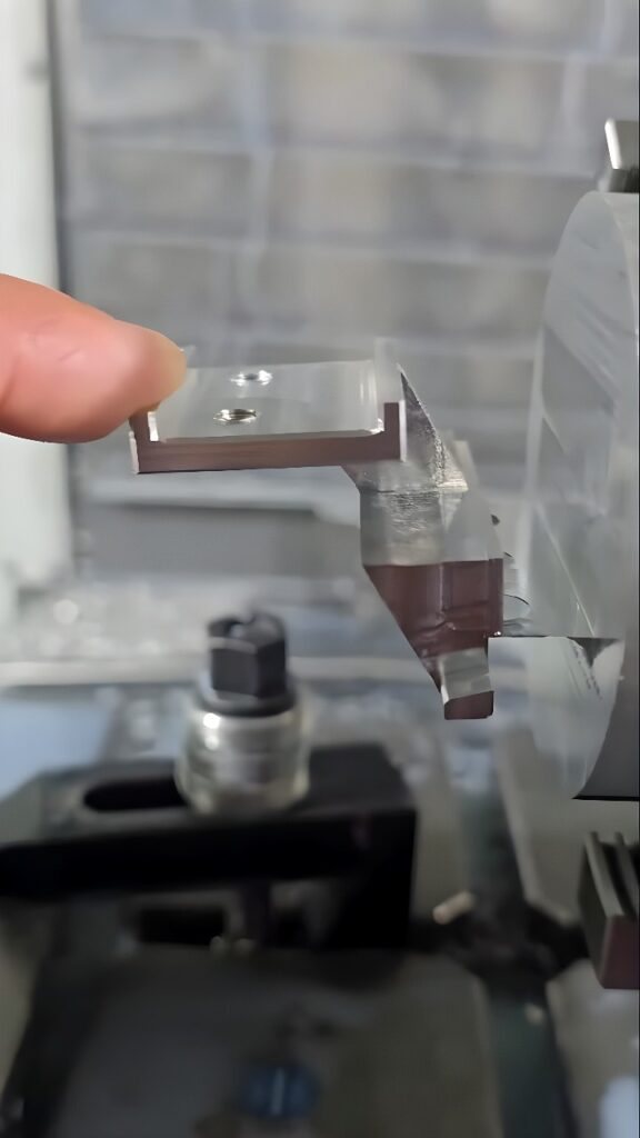 CNC machining center gripping an L-shaped aluminum bracket with finished faces and counter-bored holes