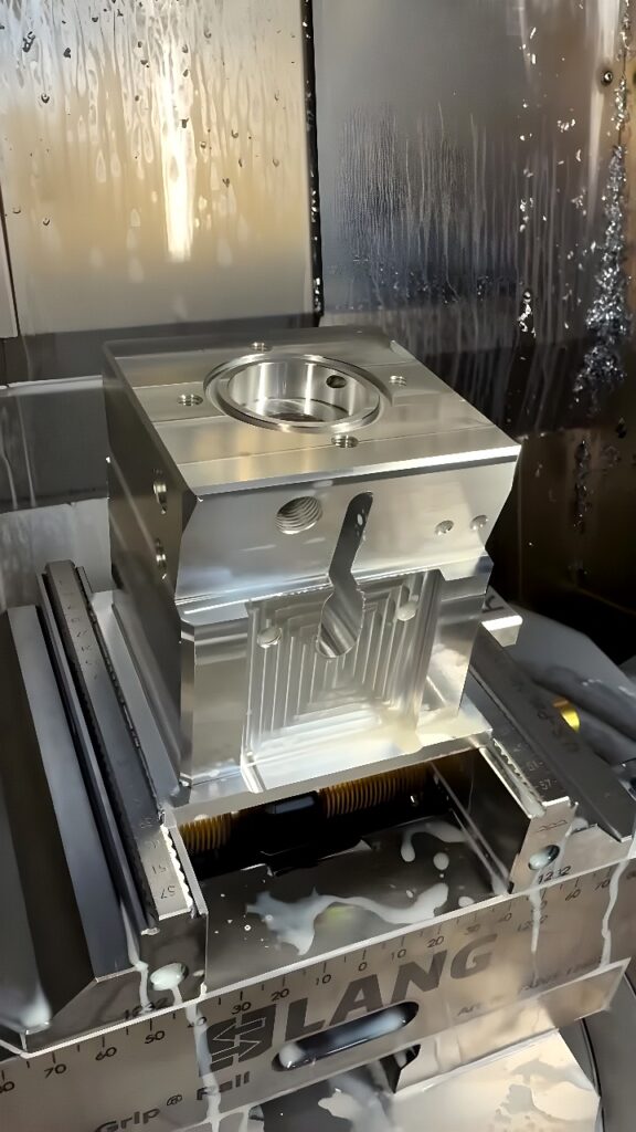 Vertical CNC milling center machining an aluminum housing block clamped in a LANG precision vise with coolant