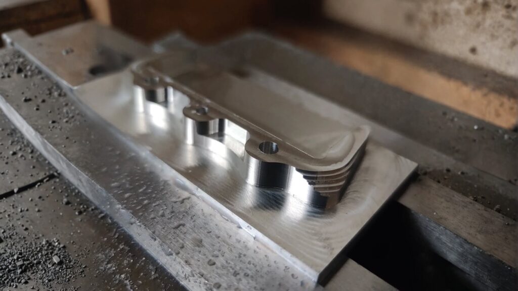 Close-up of a CNC-milled aluminum bracket with mounting holes and recesses, showing precision machining and metal finish.