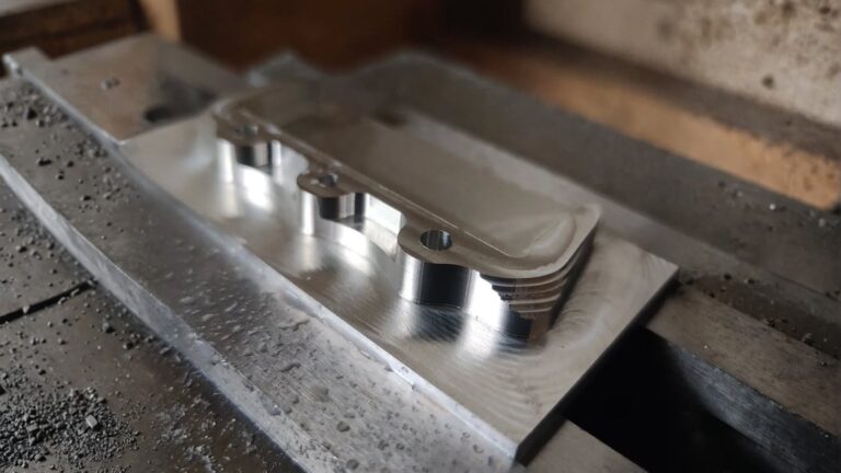 Close-up of a CNC-milled aluminum bracket with mounting holes and recesses, showing precision machining and metal finish.