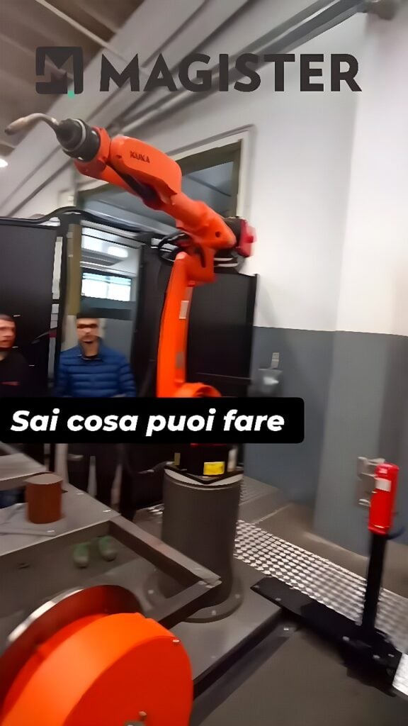 Orange KUKA six-axis robot arm with welding torch welding a cylindrical steel workpiece on a rotary fixture inside an industrial cell.
