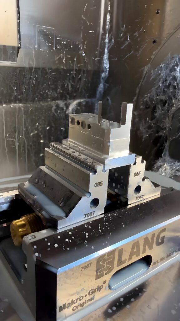 Lang Makro-Grip vise clamping an aluminum block inside a CNC machining center with coolant spray