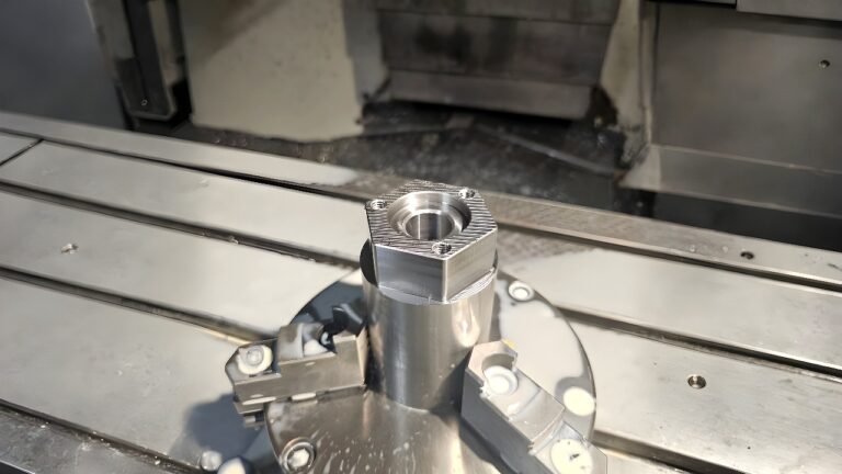 A hexagonal-ended metal part clamped in a CNC milling machine, showing fresh tool marks and precision machining.