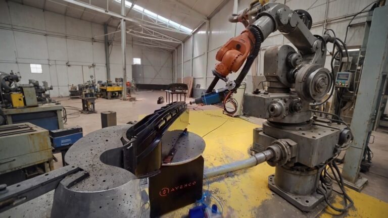 Orange industrial robot milling a black plastic rail with a blue spindle tool