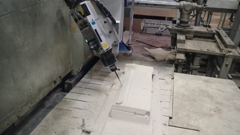 An industrial CNC router spindle milling a white foam block, shaping a cavity with fine foam dust around it.