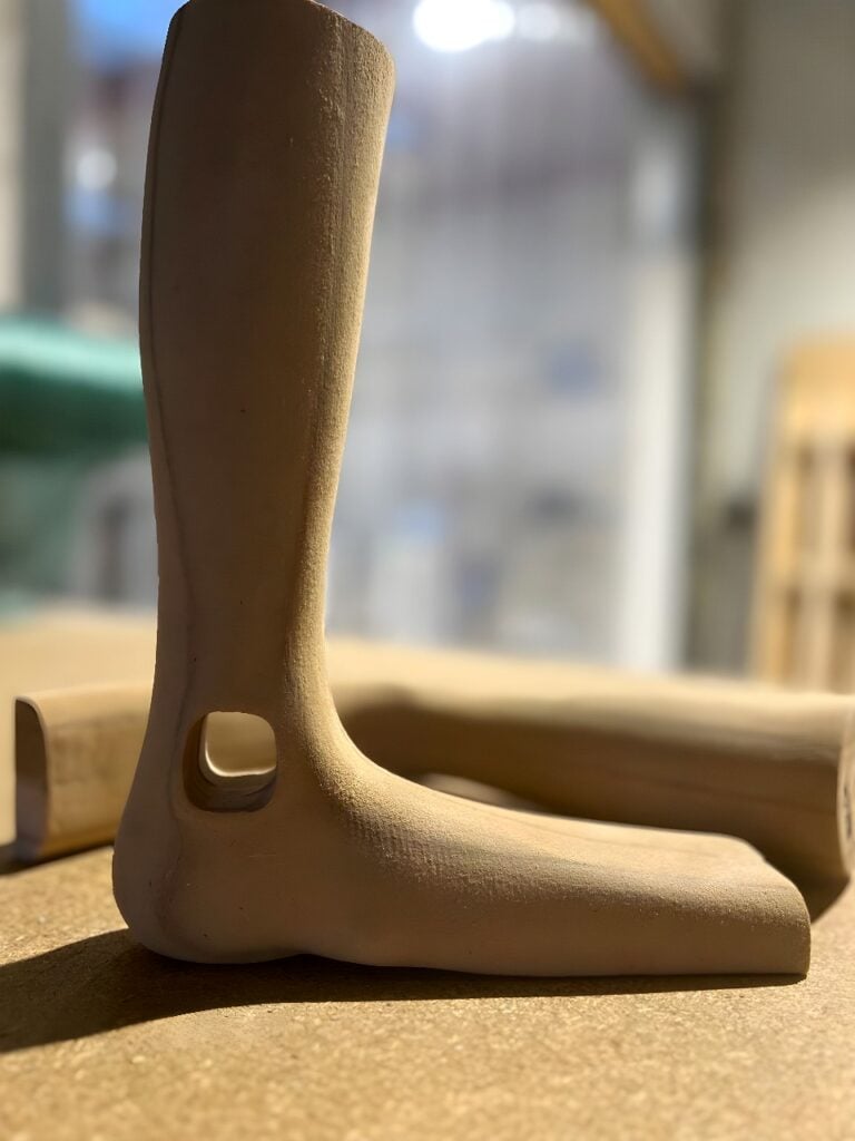 Six-axis industrial robot arm with high-speed spindle milling a light-colored foam block into a contoured prototype inside an automated machining cell