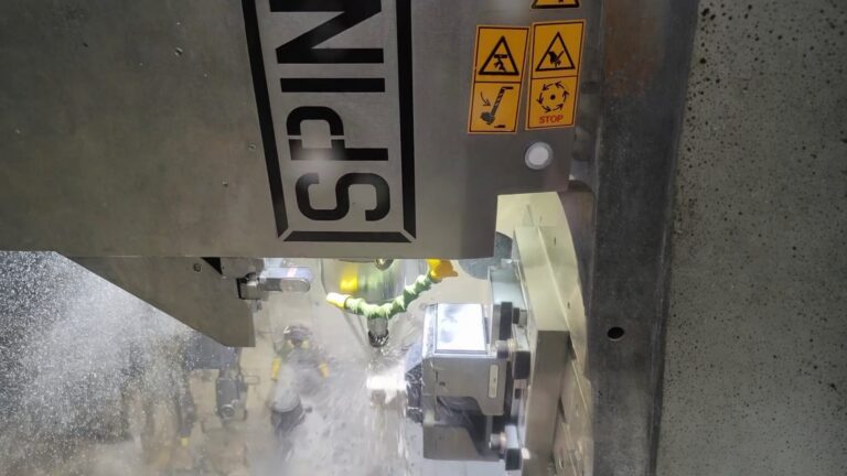 Vertical CNC machining center performing wet milling on a metal workpiece with coolant flow
