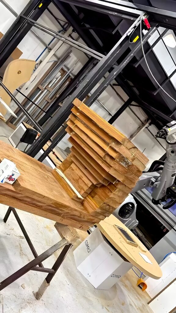 Six-axis industrial robot with spindle end effector beside a stepped wooden block assembly in a workshop