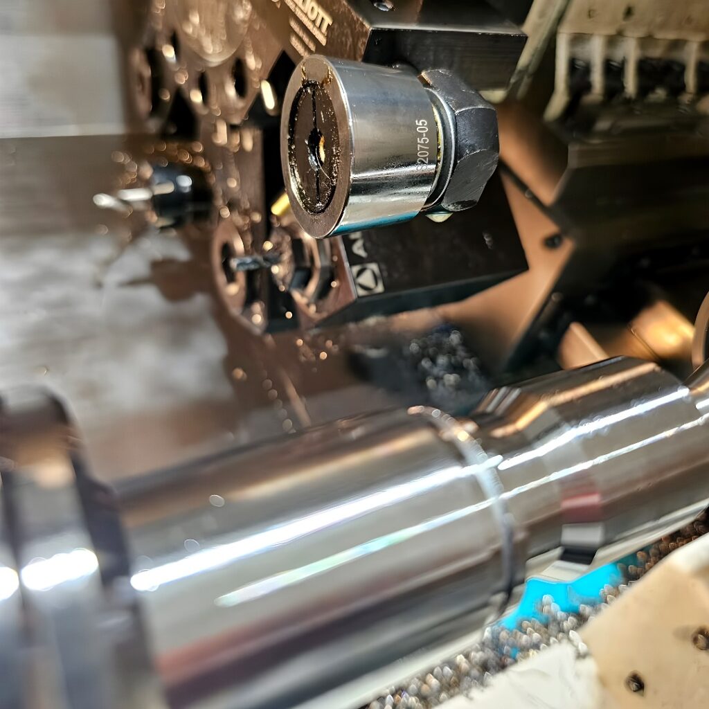 A CNC lathe performing a turning operation on a cylindrical metal shaft with a turret-mounted cutting tool.