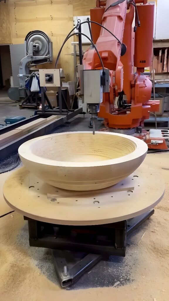 ABB six-axis industrial robot arm milling the interior of a large wooden bowl blank on a rotary table